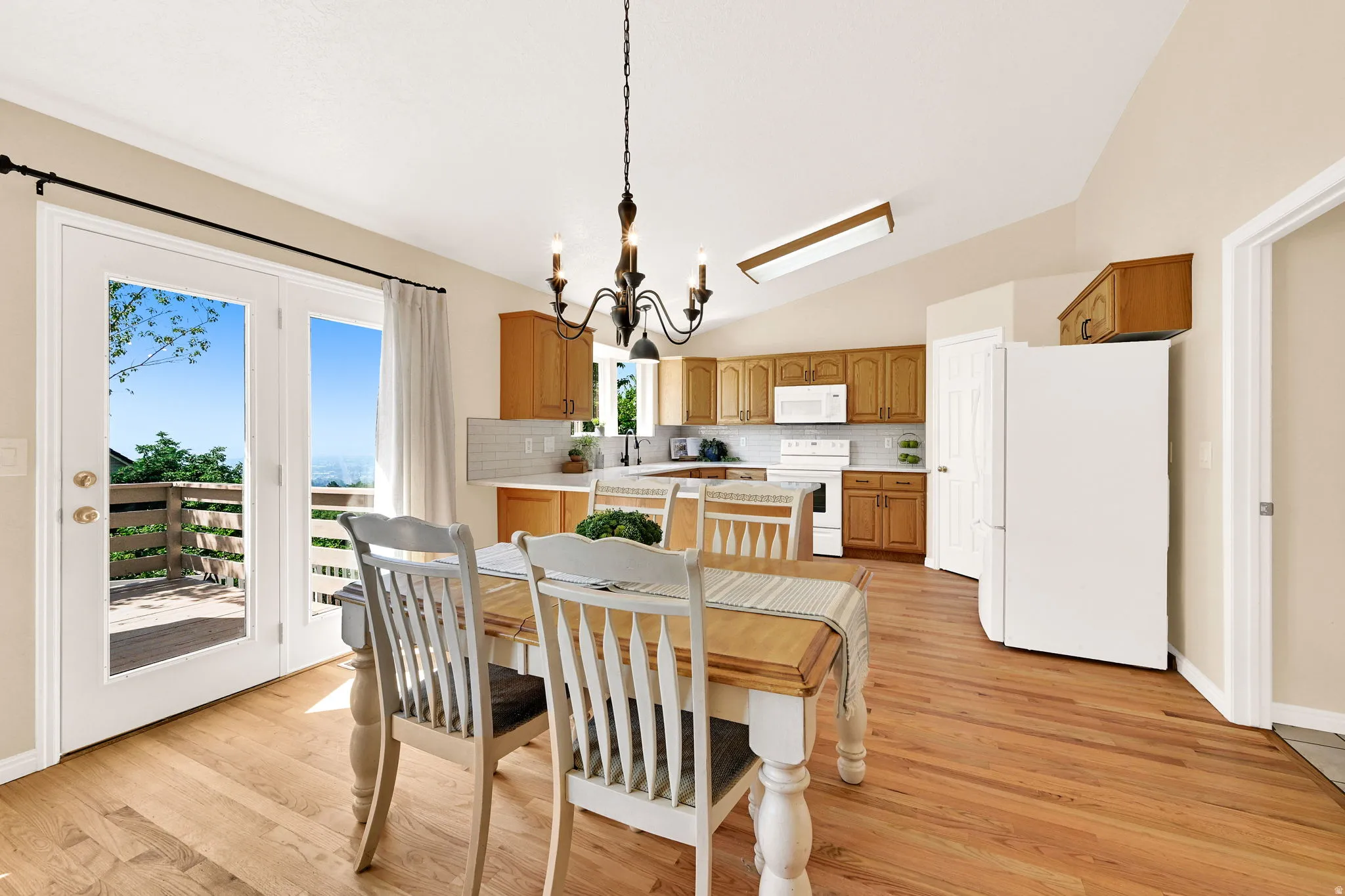 Kitchen and dining area featuring wood-finish flooring, white French doors opening to a deck, and a vaulted ceiling with a chandelier