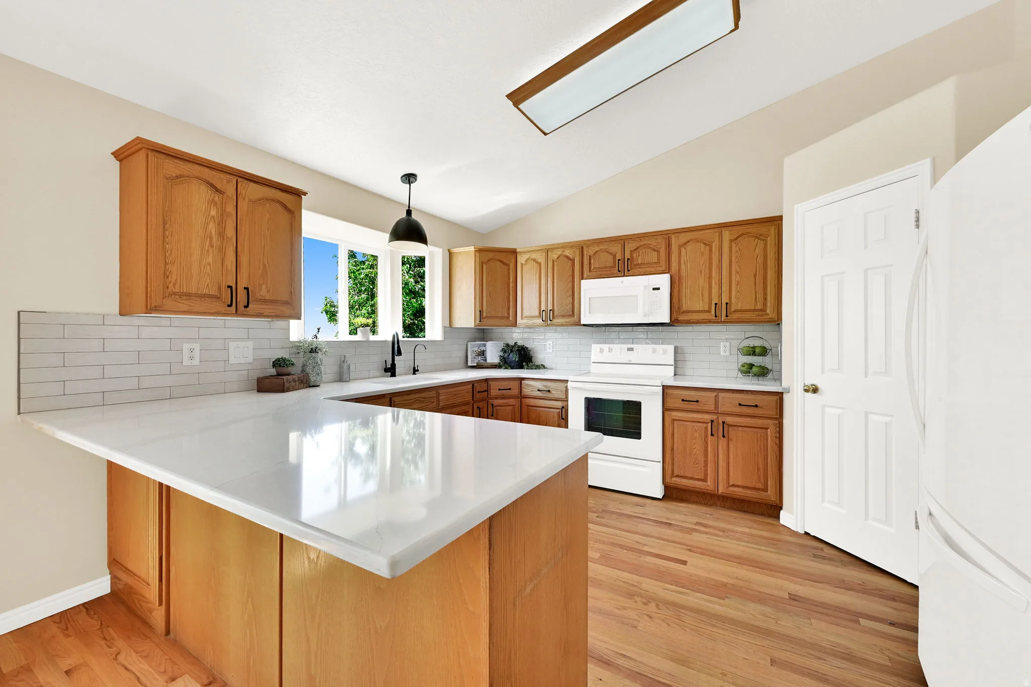 Kitchen featuring light wood cabinetry, white countertops, white subway tile backsplash, and wood-finish flooring