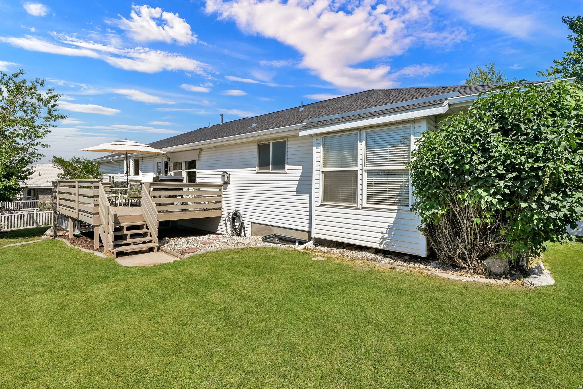 Spacious backyard featuring a wooden deck with railing, stairs, and a gravel border