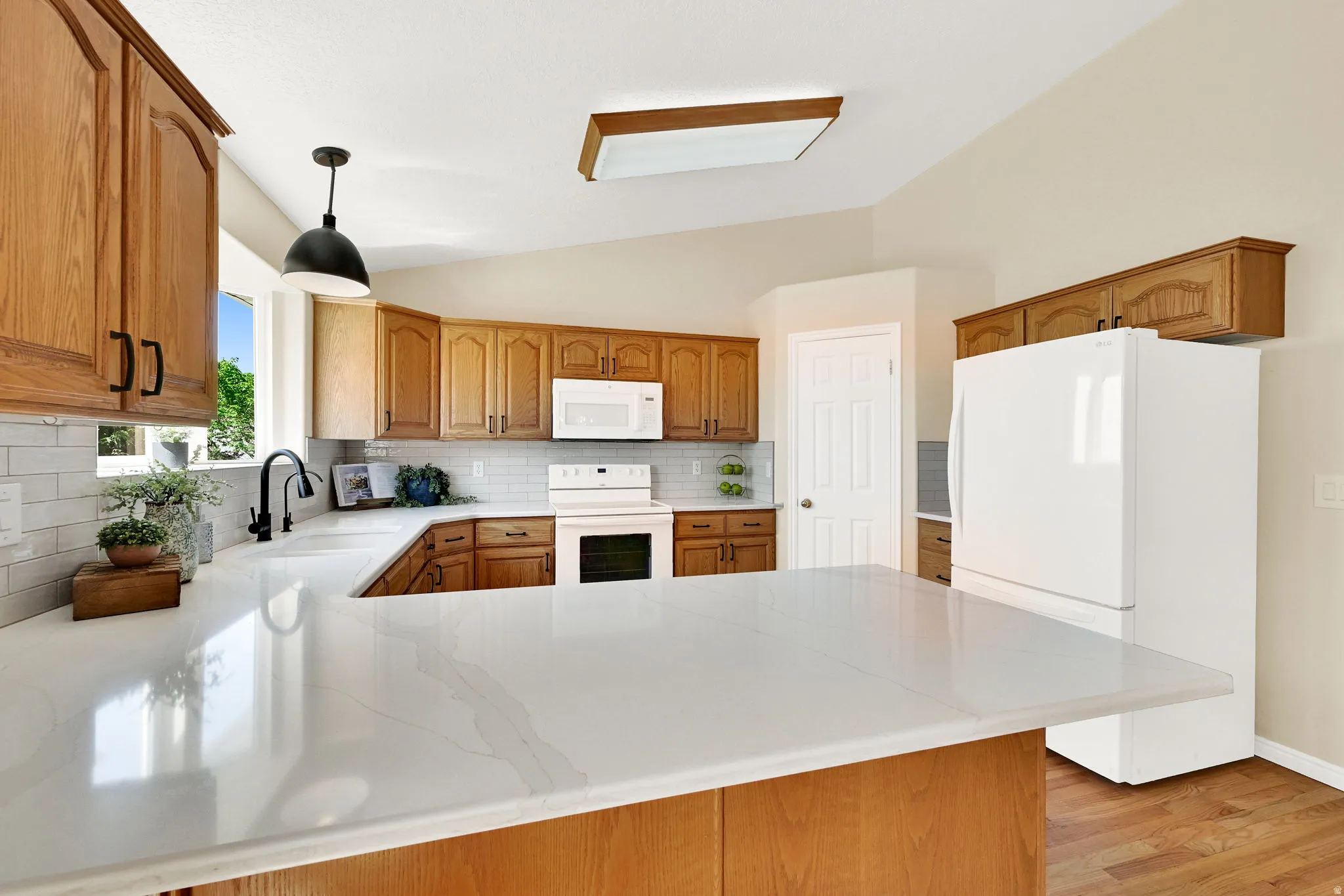 Kitchen featuring light wood cabinetry, white countertops, a subway tile backsplash, and wood-finish flooring