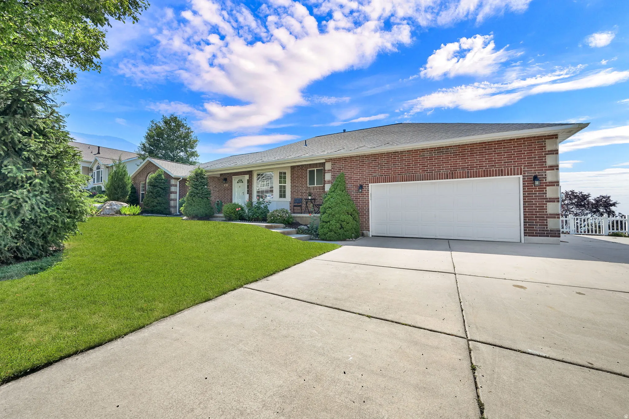 Brick exterior with a prominent two-car garage, concrete driveway, front lawn, and foundational plantings