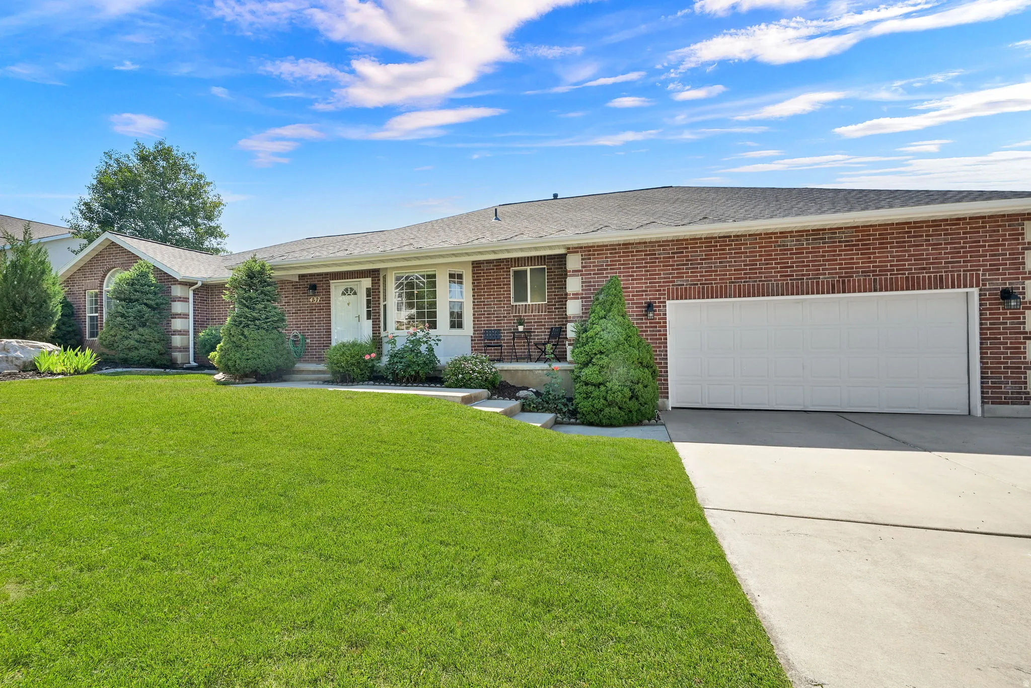 Brick exterior featuring a two-car garage, mature landscaping, and a bay window