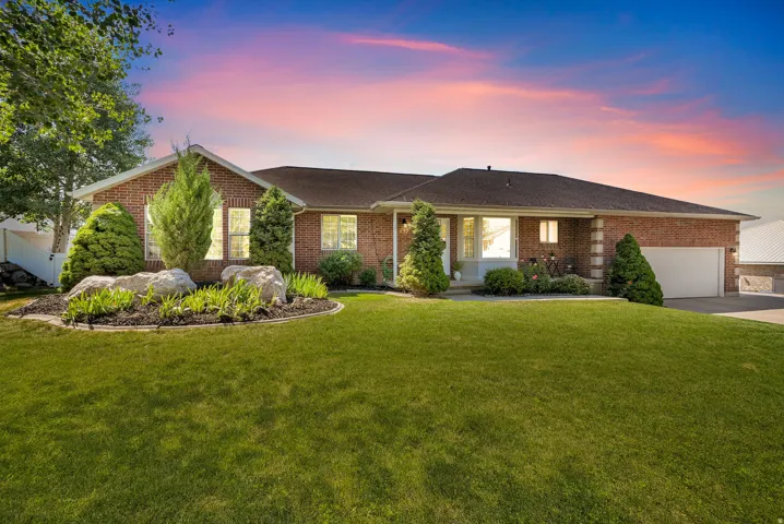 Traditional brick exterior featuring a manicured front lawn, established landscaping with large decorative rocks, a two-car garage with an automatic door, and multiple large windows