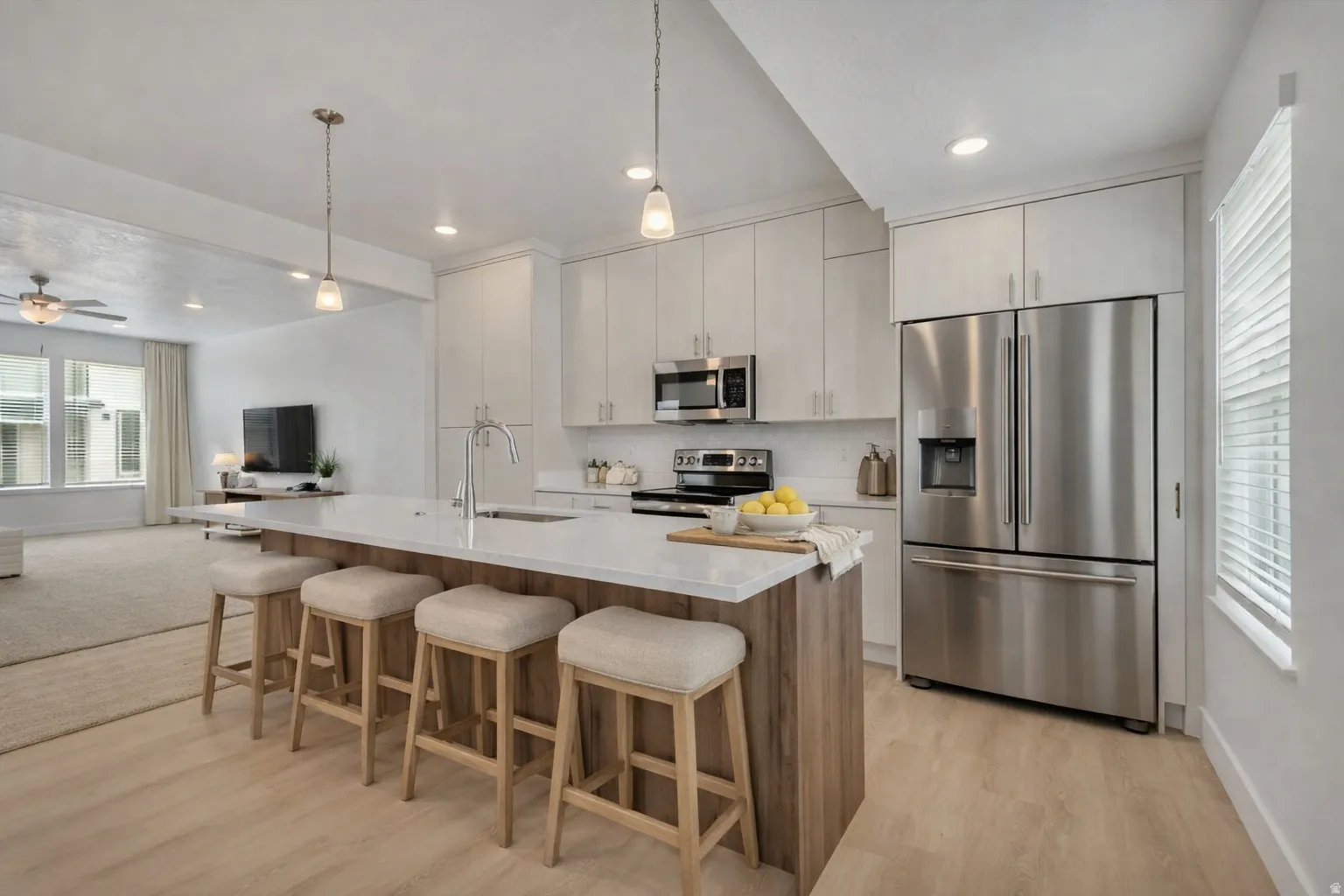 Modern kitchen featuring a spacious island with seating, stainless steel appliances, light-toned cabinetry, wood-finish flooring, and recessed lighting