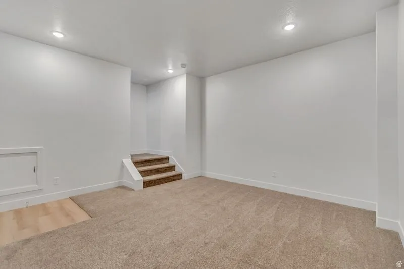Spacious room featuring neutral carpeting, recessed lighting, white baseboards, and a three-step carpeted staircase
