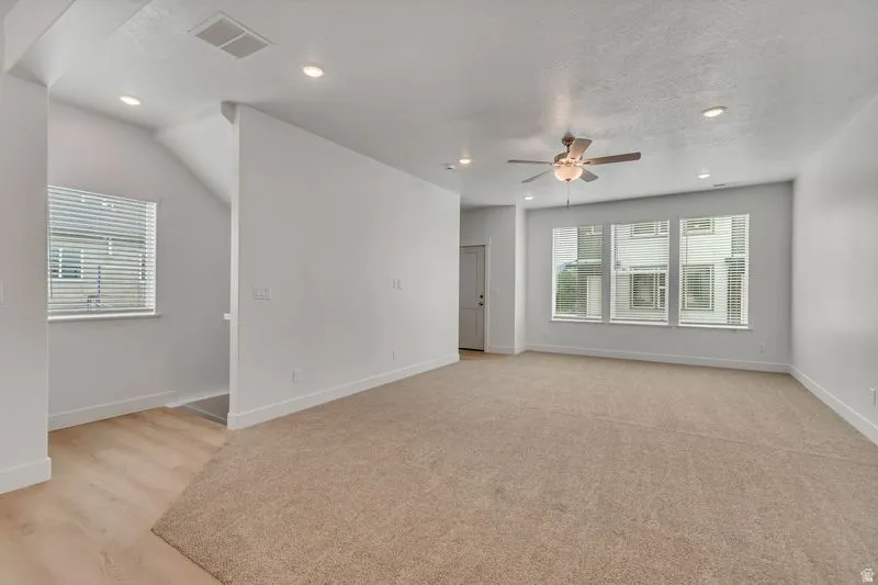 Spacious living area featuring neutral carpeting, recessed lighting, and a ceiling fan