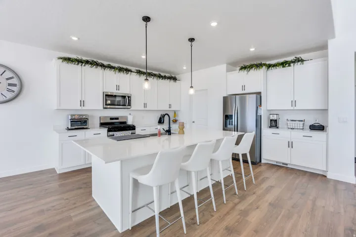 Contemporary kitchen featuring an oversized island with seating, white shaker cabinetry, stainless steel appliances, recessed lighting, and wood-finish flooring