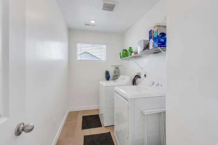 Dedicated laundry space featuring neutral-toned tile flooring, white walls, and a small window with horizontal blinds