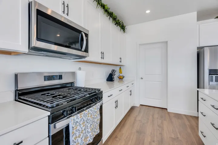 Modern kitchen featuring white cabinetry, stone-finish countertops, stainless steel appliances, and wood-finish flooring