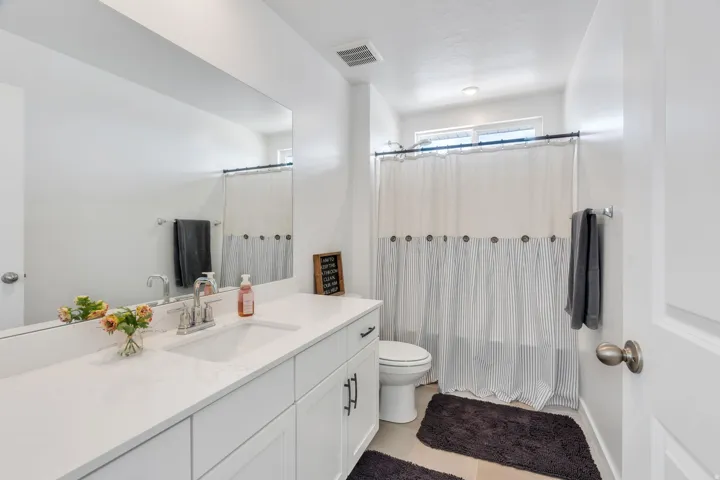 Bathroom featuring a white vanity with an integrated rectangular sink, a large mirror, and a built-in tub with shower