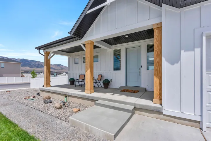 Modern farmhouse exterior featuring board and batten siding, a covered front porch with natural wood-finish columns, a light-colored entry door, and concrete steps