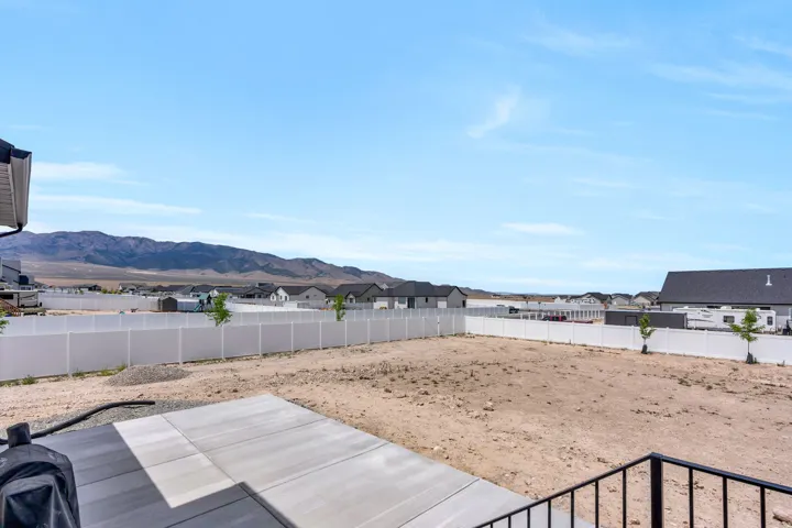 Expansive backyard space featuring a concrete patio, white vinyl fencing, and distant mountain scenery