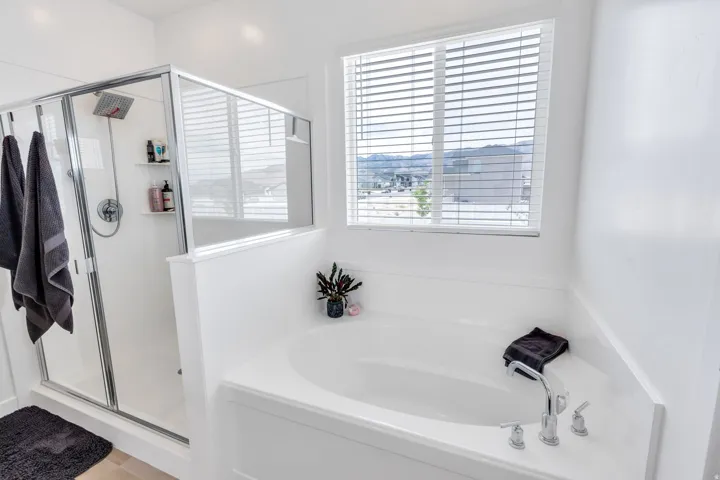 White soaking tub with chrome fixtures, accompanied by a glass-enclosed shower featuring a square rainfall showerhead and built-in shelving