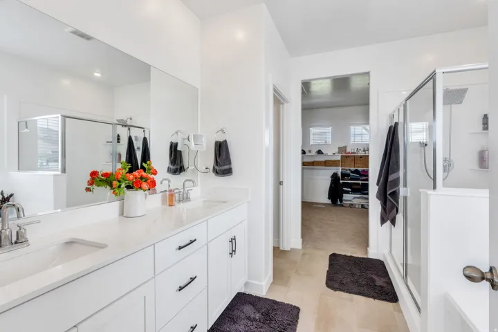 Spacious bathroom featuring a dual vanity with white cabinetry and light-toned countertops, a large frameless mirror, and a glass-enclosed shower with a rainfall showerhead