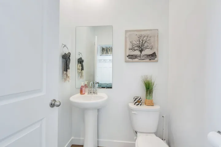 Pedestal sink with chrome faucet, a rectangular mirror, and wood-finish flooring