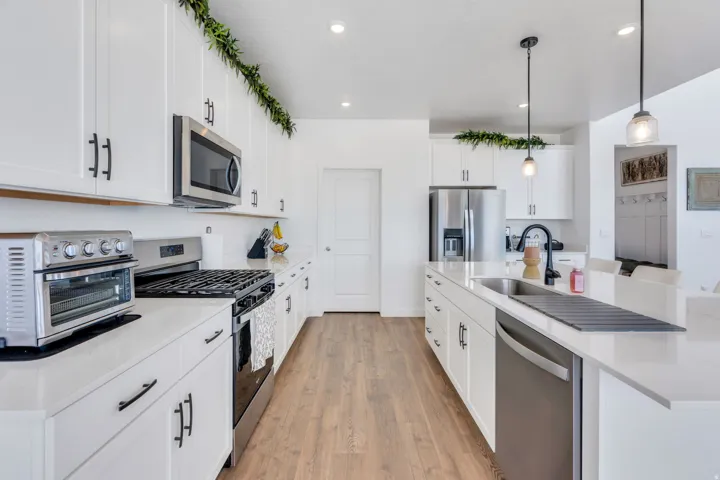 Modern kitchen featuring white cabinetry, stainless steel appliances, wood-finish flooring, and white countertops