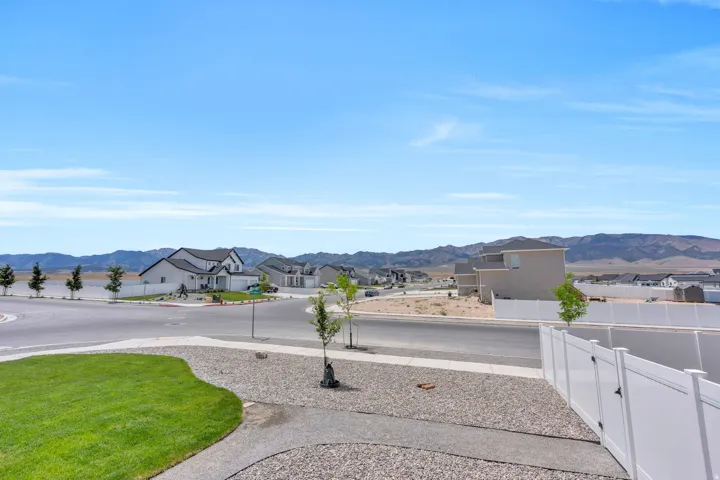 Landscaped front yard with a manicured lawn area and gravel accents, featuring a white vinyl fence and a distant mountain backdrop