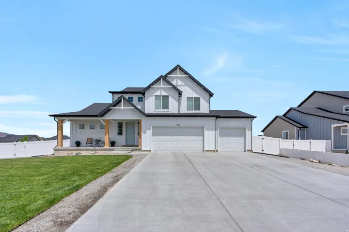 Modern farmhouse exterior featuring white vertical siding, a dark pitched roof, and a covered porch with natural wood columns
