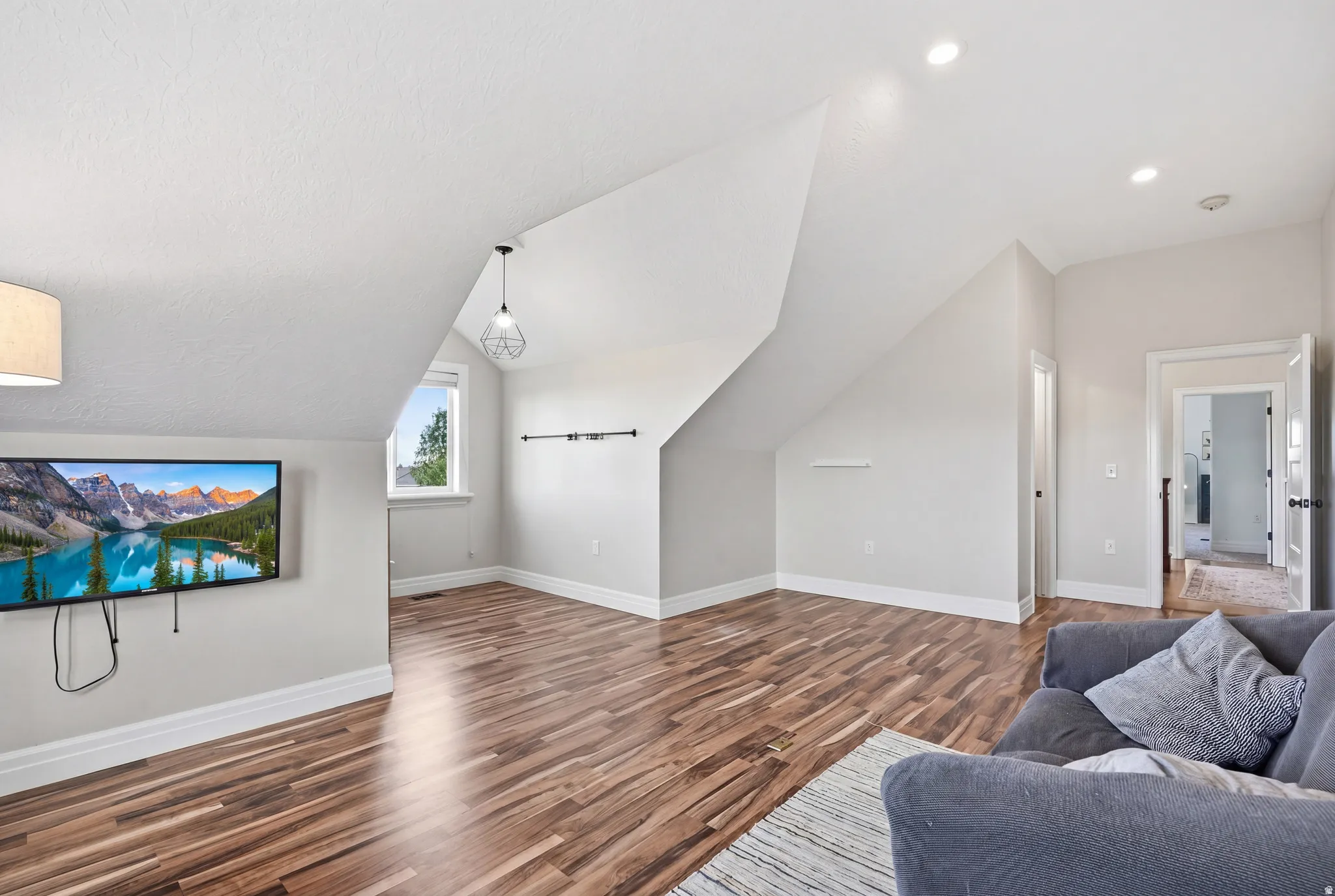 Spacious room featuring wood-finish flooring, a wall-mounted television, and a window for natural light