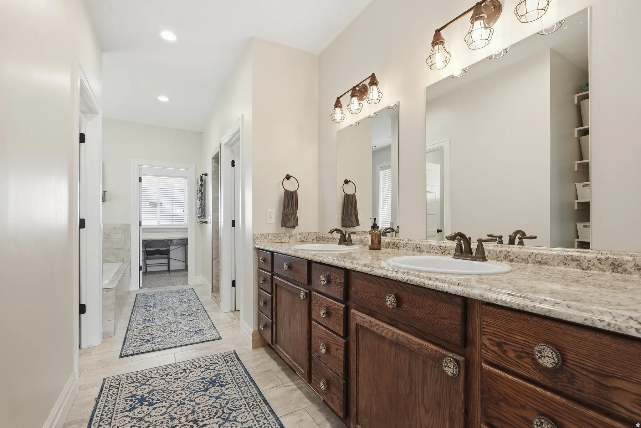 Double vanity featuring wood-finish cabinetry with decorative hardware, dual undermount sinks, and a light-toned countertop