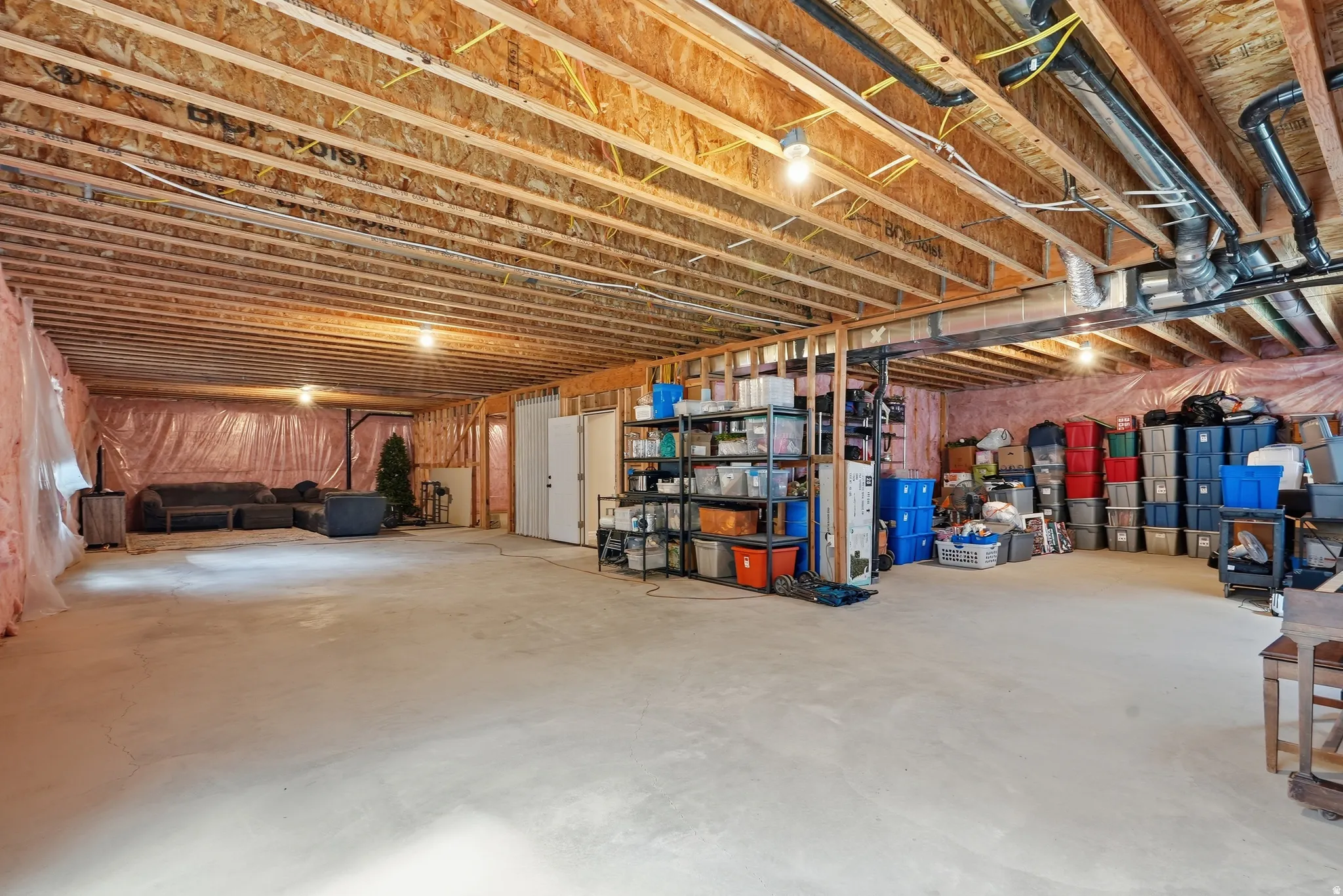 Expansive unfinished basement featuring an open floor plan, exposed wood joists, concrete flooring, and insulated walls
