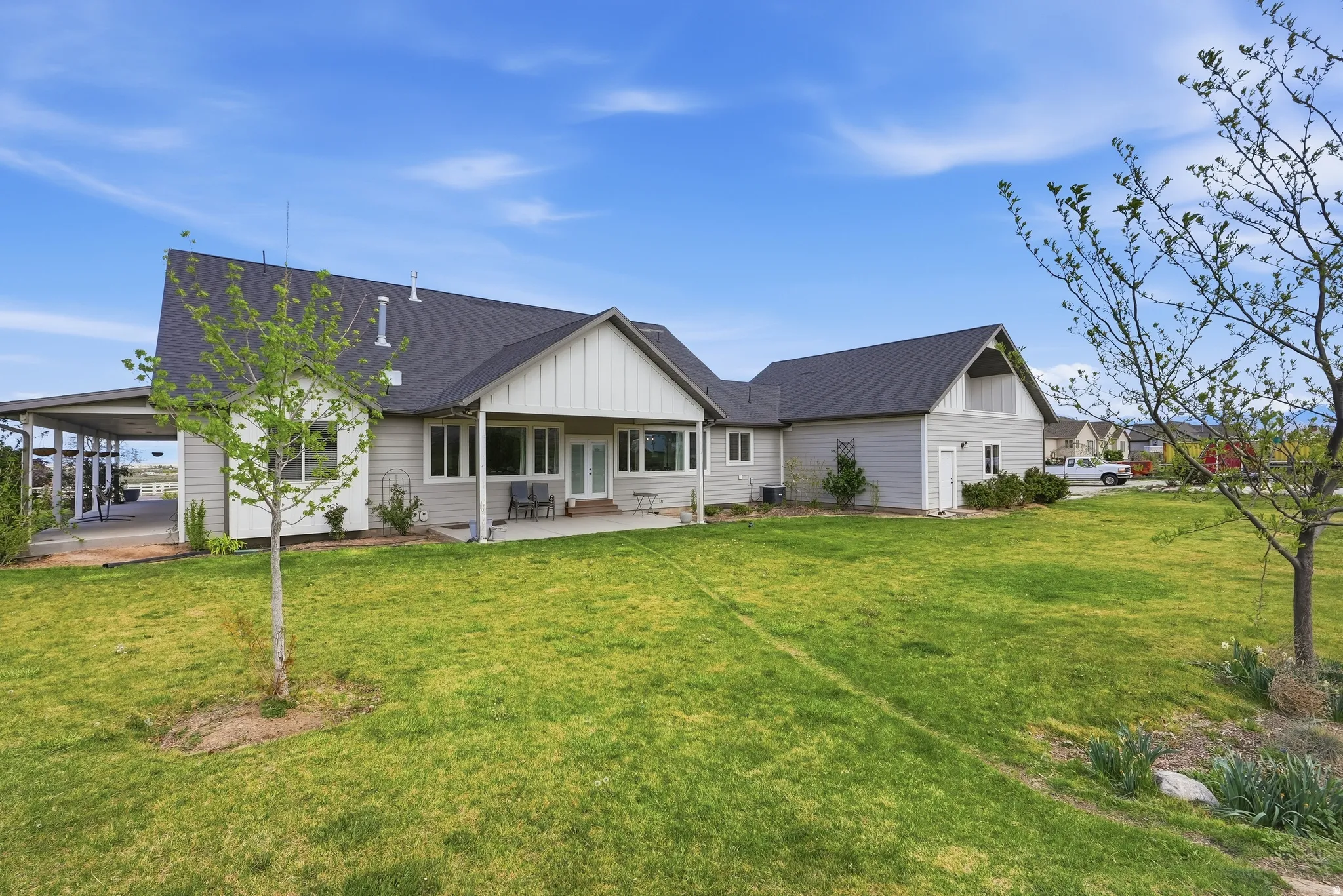 Expansive rear yard featuring a concrete patio, covered carport, and mature landscaping