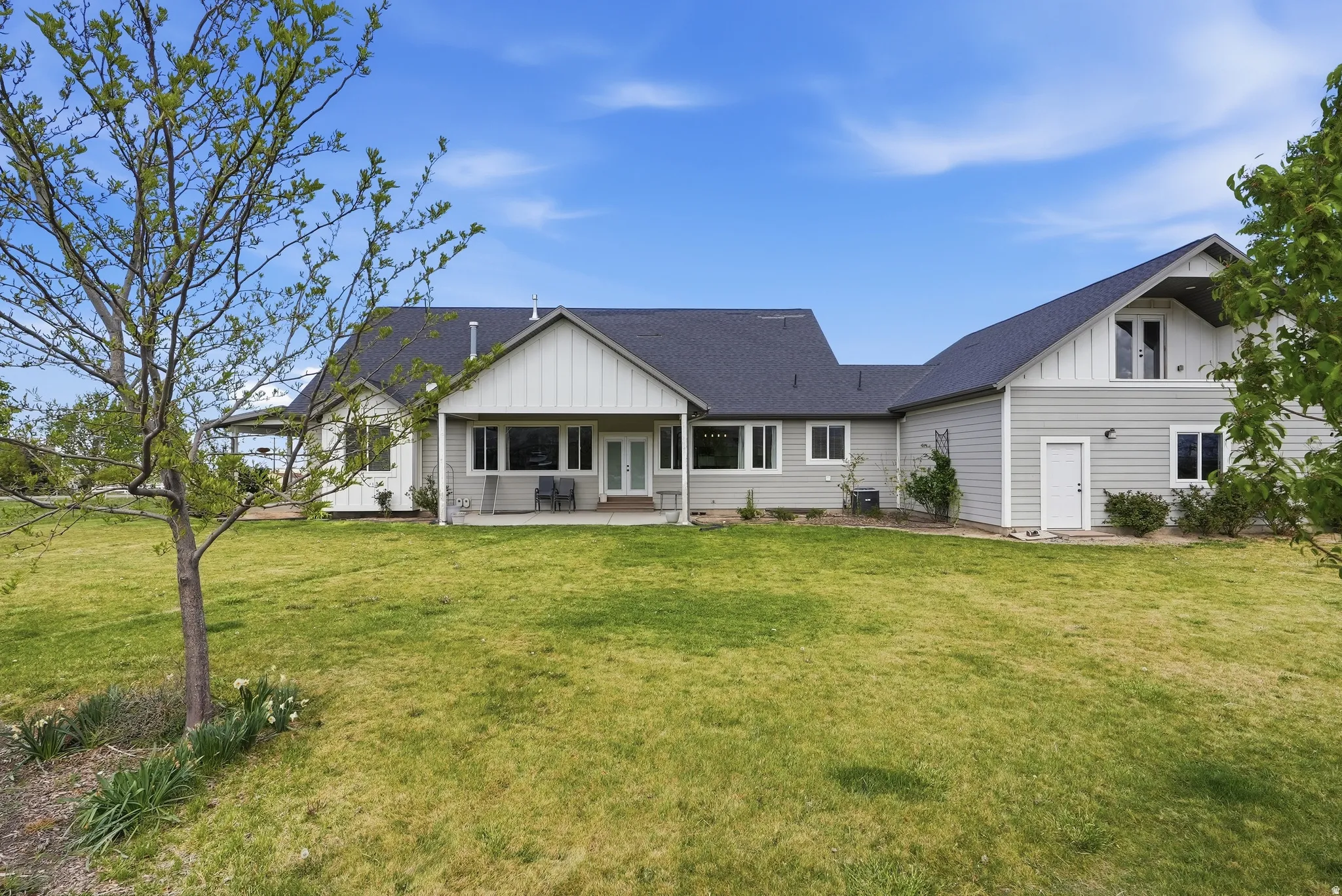 Rear exterior featuring gray horizontal siding, white vertical siding accents, dark shingled roofing, a covered patio, and multiple windows
