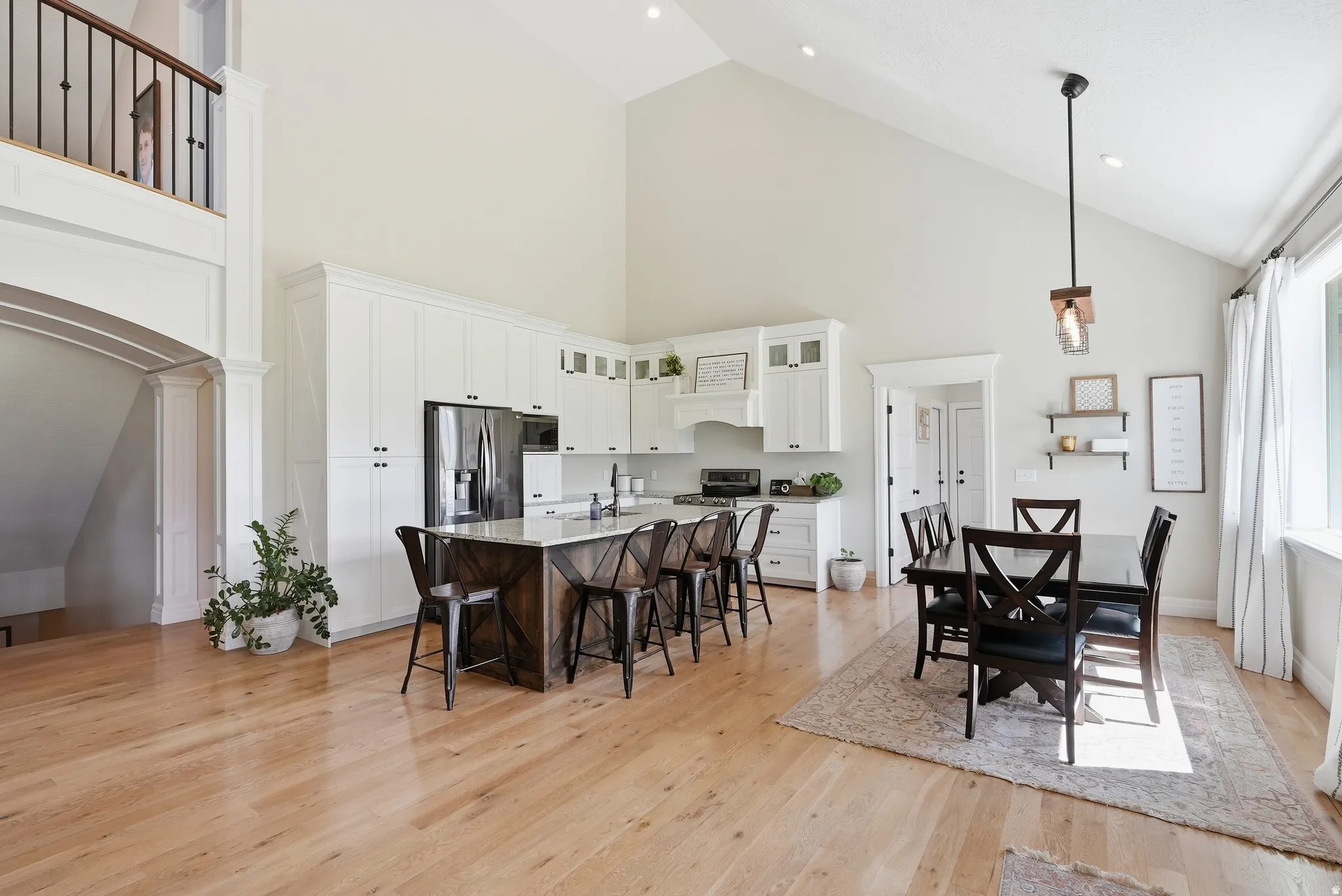 Vaulted ceiling kitchen featuring white cabinetry, stainless steel appliances, a center island with a light-toned countertop, and wood-finish flooring