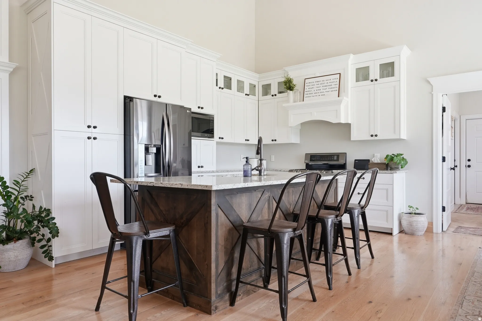Kitchen featuring a large island with a stone-finish countertop, white cabinetry, integrated stainless steel refrigerator, and wood-finish flooring