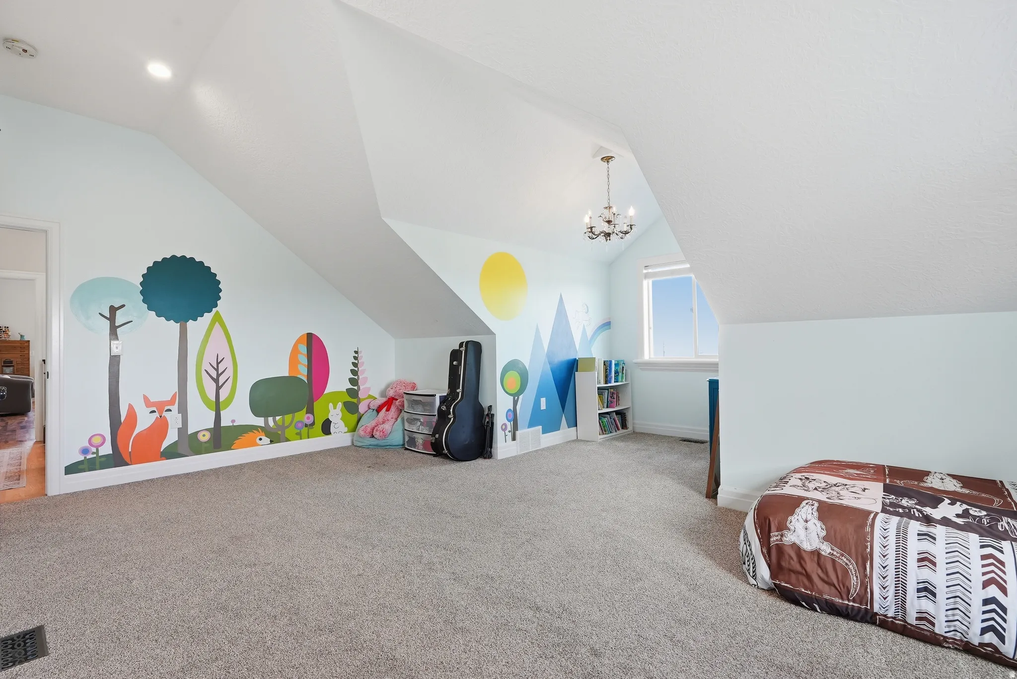 Expansive carpeted room featuring sloped ceilings, wall-mounted lighting, and a window with natural light