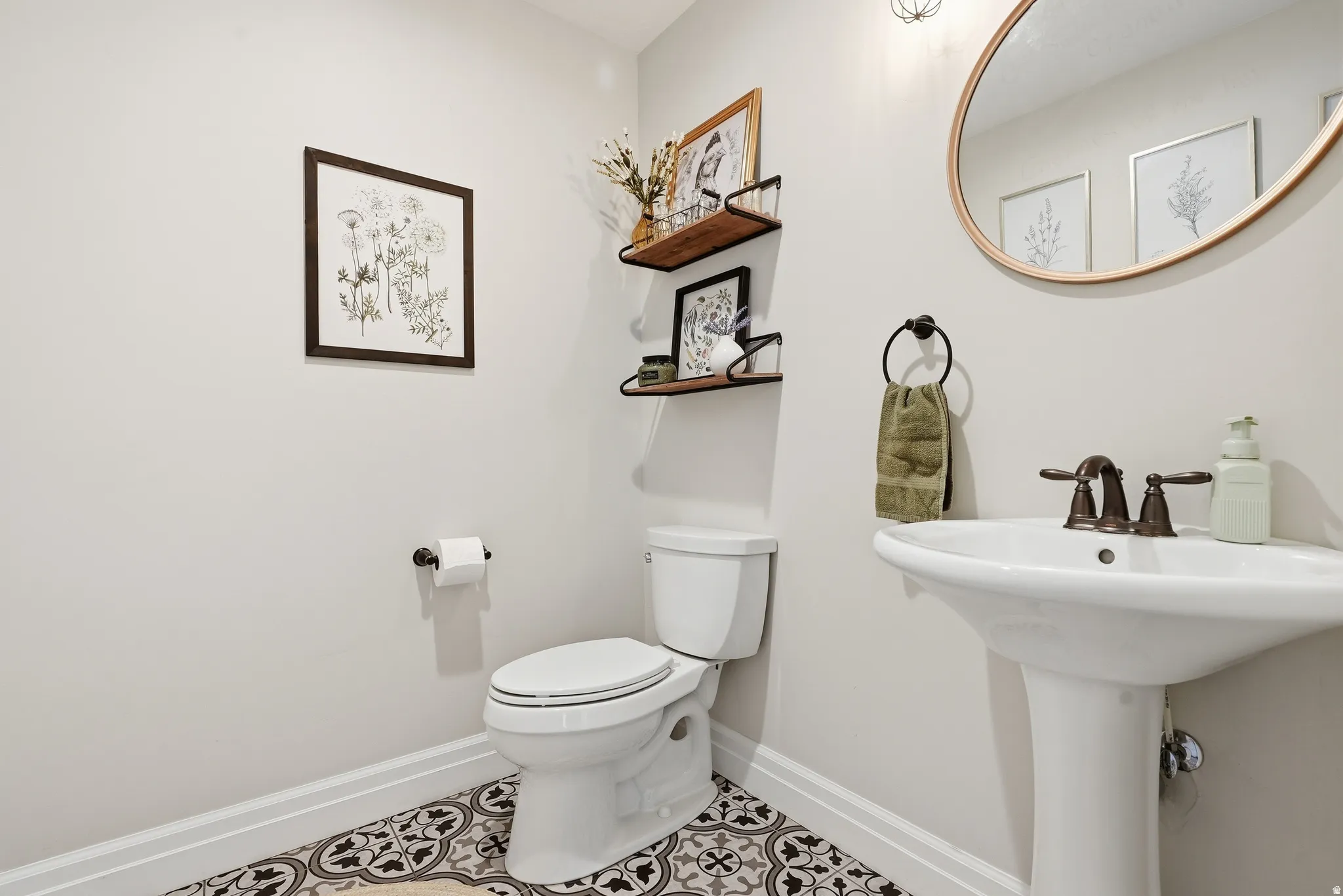 Pedestal sink with bronze-finish faucet, accompanied by a toilet and patterned floor tile