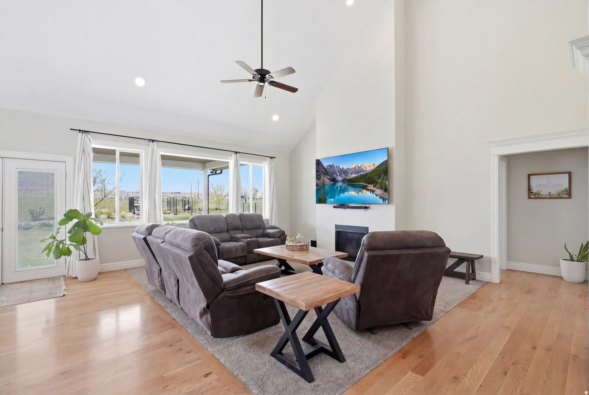 Light wood-finish flooring, vaulted ceilings, and a ceiling fan with integrated lighting