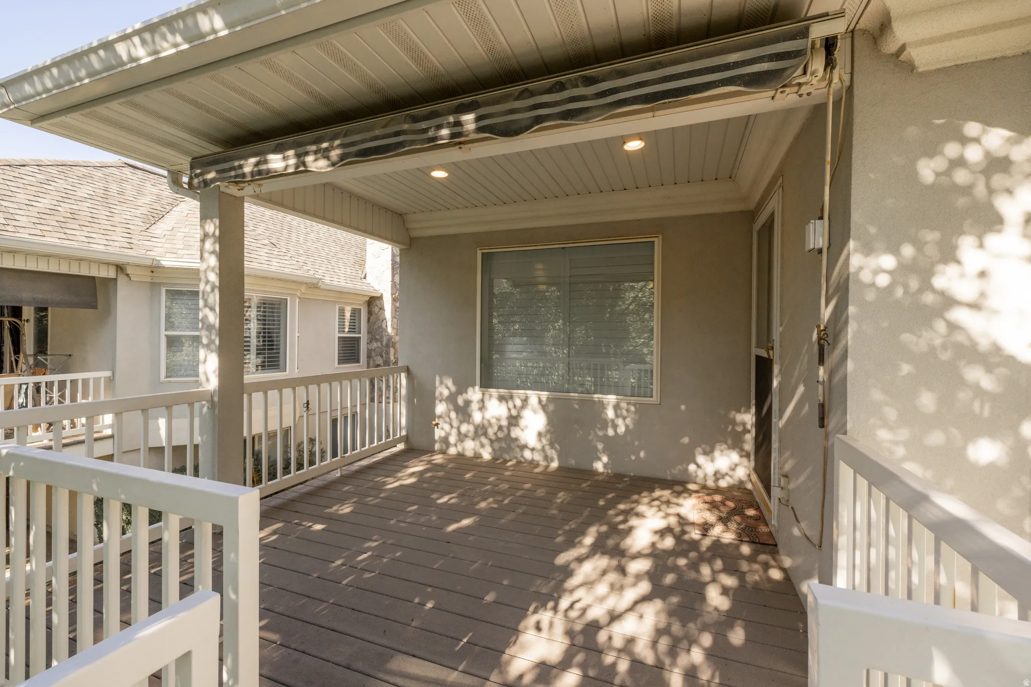 Covered outdoor deck featuring composite decking, white railing, recessed lighting, and stucco exterior walls