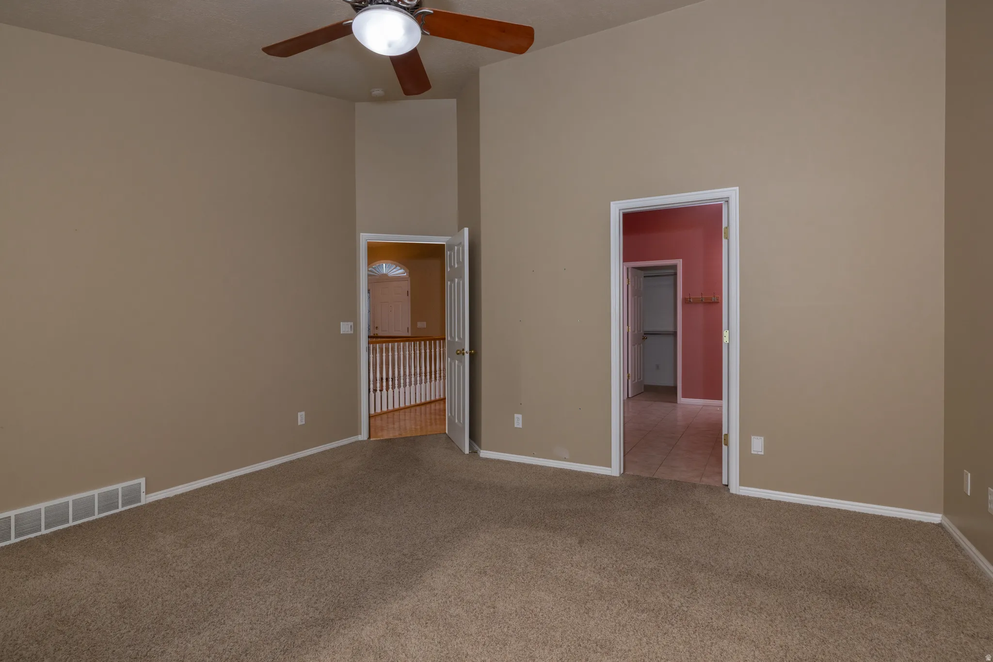 Carpeted room featuring a ceiling fan, vaulted ceiling, and two doorways