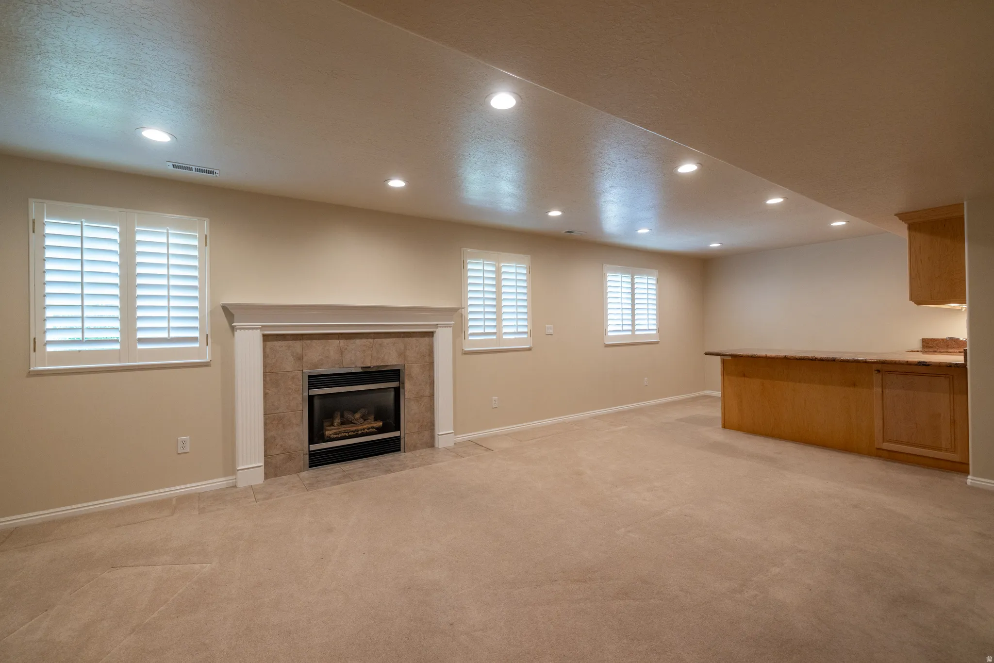 Recessed lighting illuminates a spacious room featuring a built-in fireplace with a tile surround and white mantel