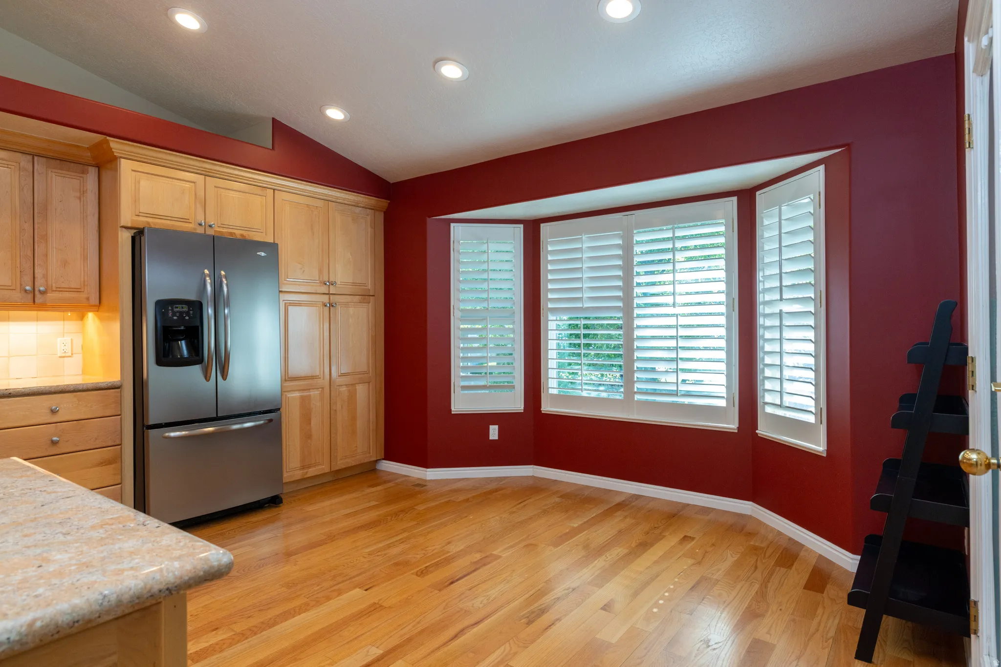 Kitchen area featuring a stainless steel French door refrigerator, wood-finish flooring, and a bay window with plantation shutters