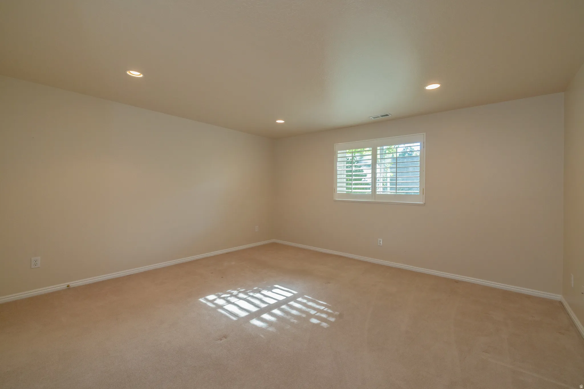 Carpeted room with recessed lighting and a window featuring white plantation shutters