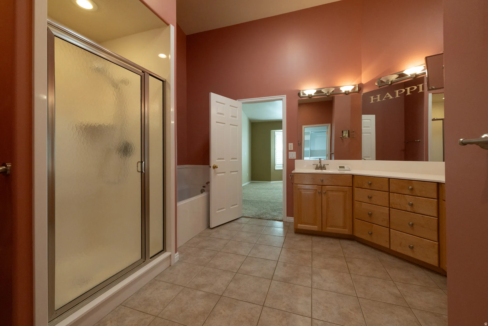 Bathroom featuring a glass-enclosed shower, a separate bathtub, a light wood-finish vanity with a single sink, an expansive mirror, and tile flooring
