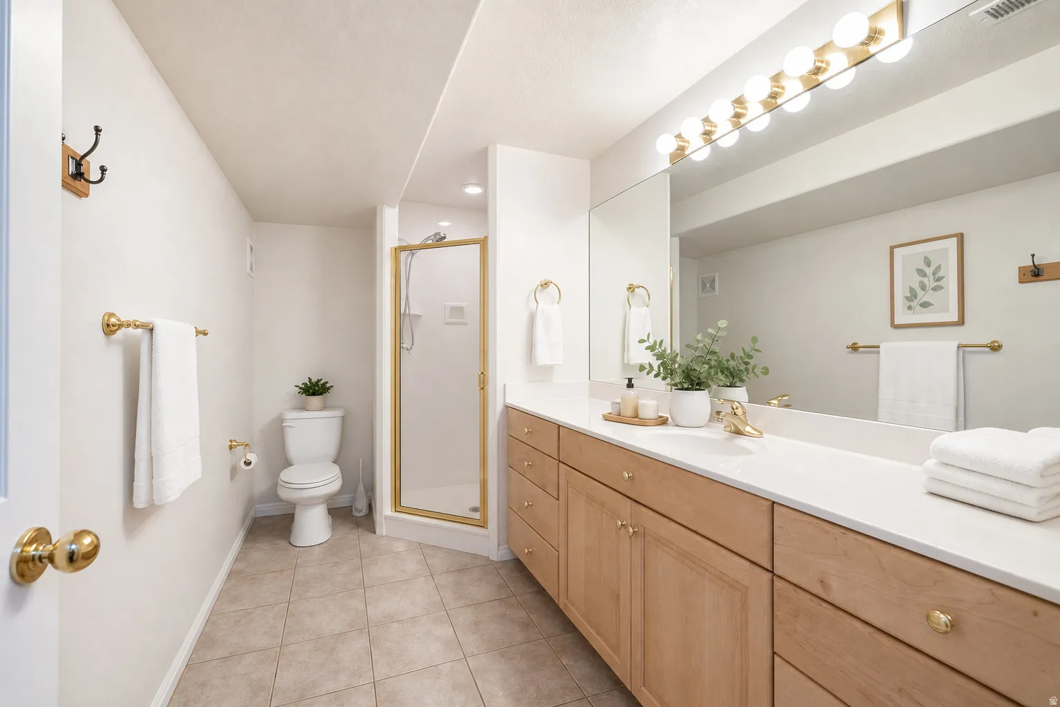 Virtually Staged - Spacious bathroom featuring an extended wood-finish double vanity with white countertops, a large vanity mirror, and a gold-framed glass shower enclosure