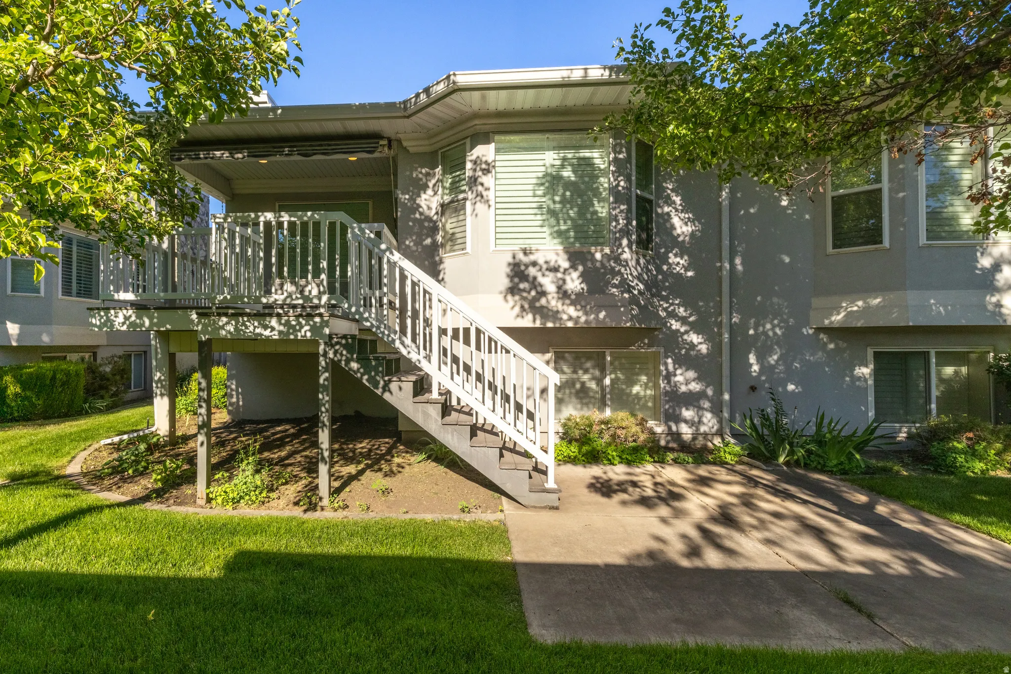 Rear exterior featuring a multi-level deck with white railings and stairs, a concrete patio, and a manicured lawn