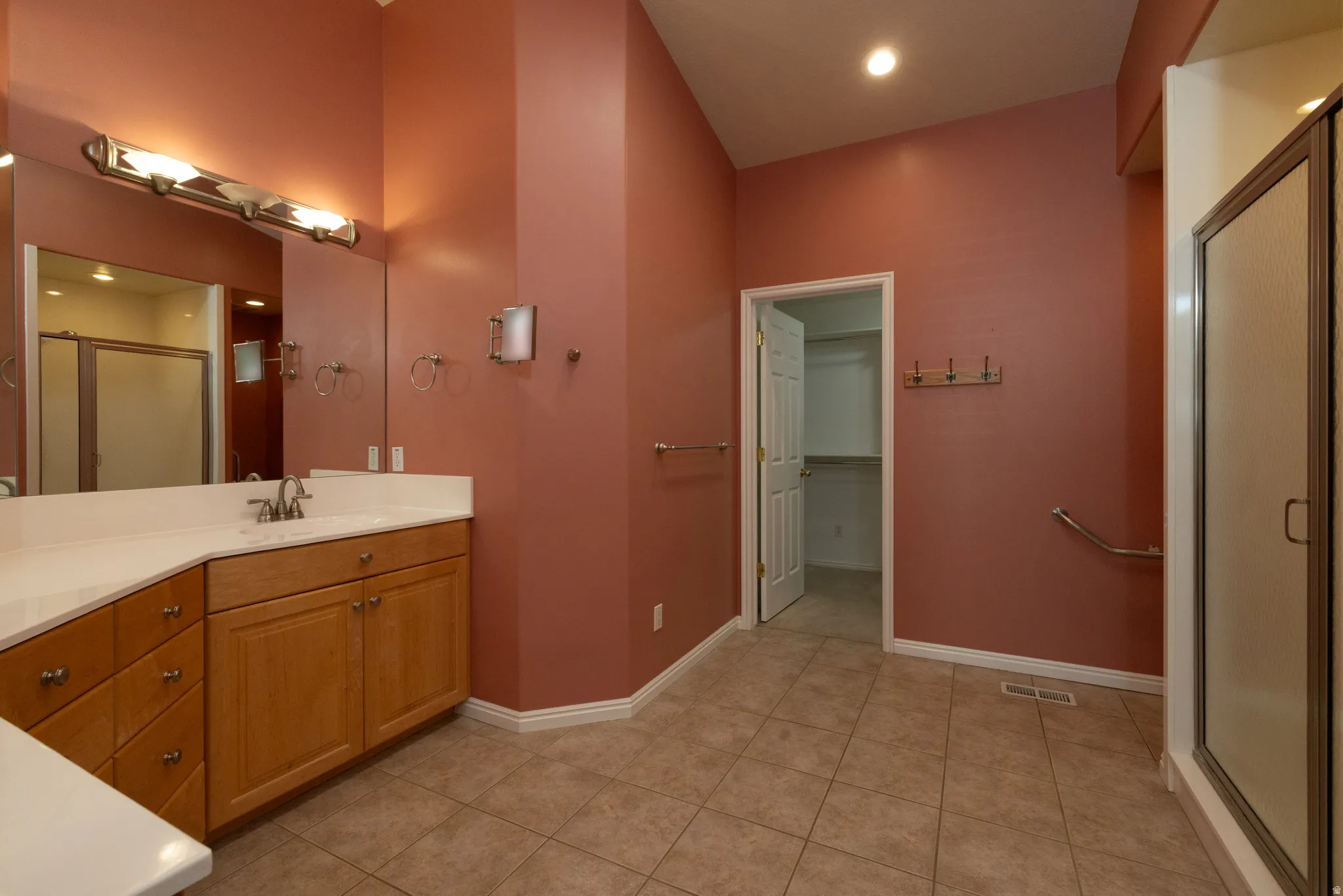 Full bathroom featuring a wood-finish vanity with a white countertop and integrated sink, a large wall mirror with overhead lighting, a shower enclosure, and neutral-toned tile flooring