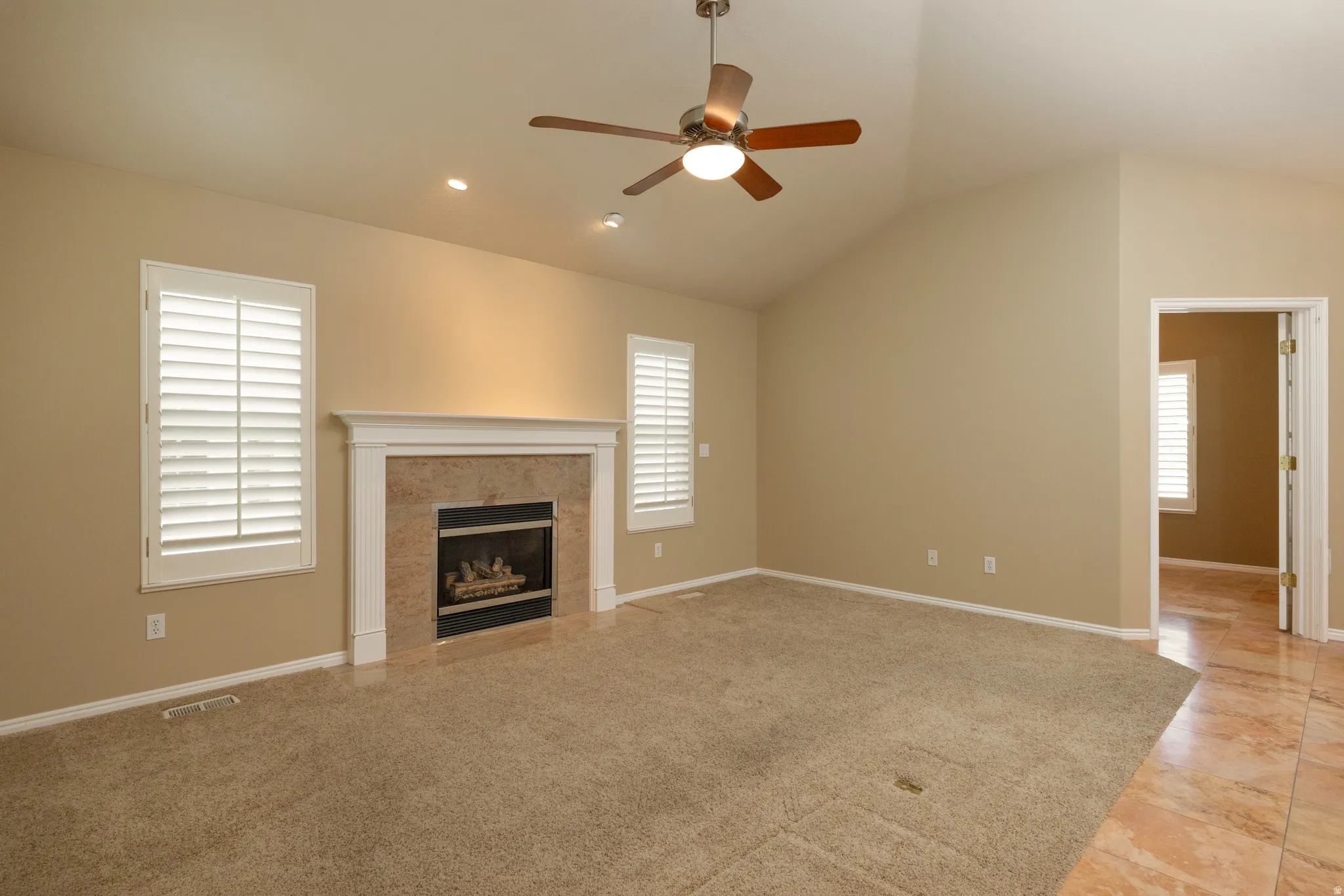 Living area featuring a textured fireplace with white mantel, vaulted ceiling, and a ceiling fan with integrated lighting