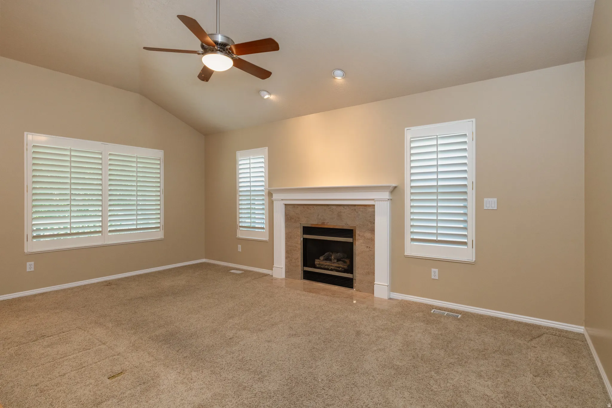 Spacious room featuring vaulted ceilings, a central fireplace with stone surround and white mantel, and ceiling fan with integrated lighting