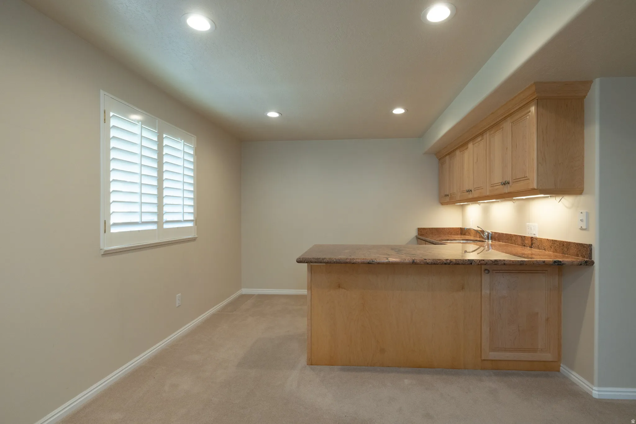 Built-in wet bar featuring light wood cabinetry, a sink, and a stone-finish countertop