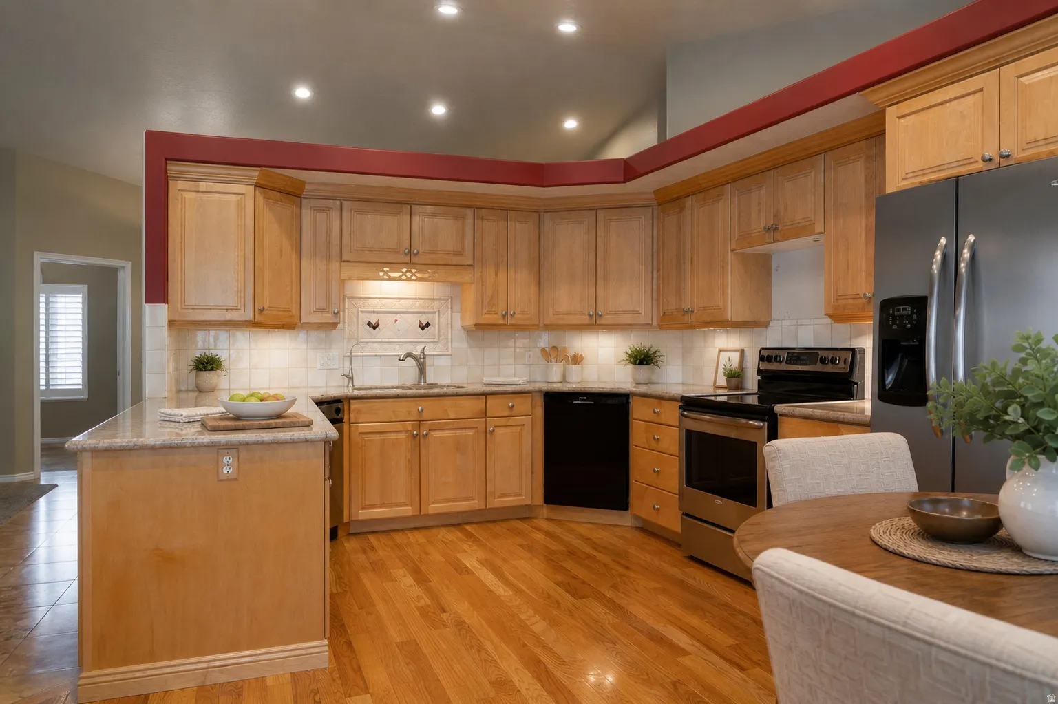 Virtually Staged - Kitchen featuring light wood cabinetry, stainless steel appliances, a tile backsplash, and wood-finish flooring