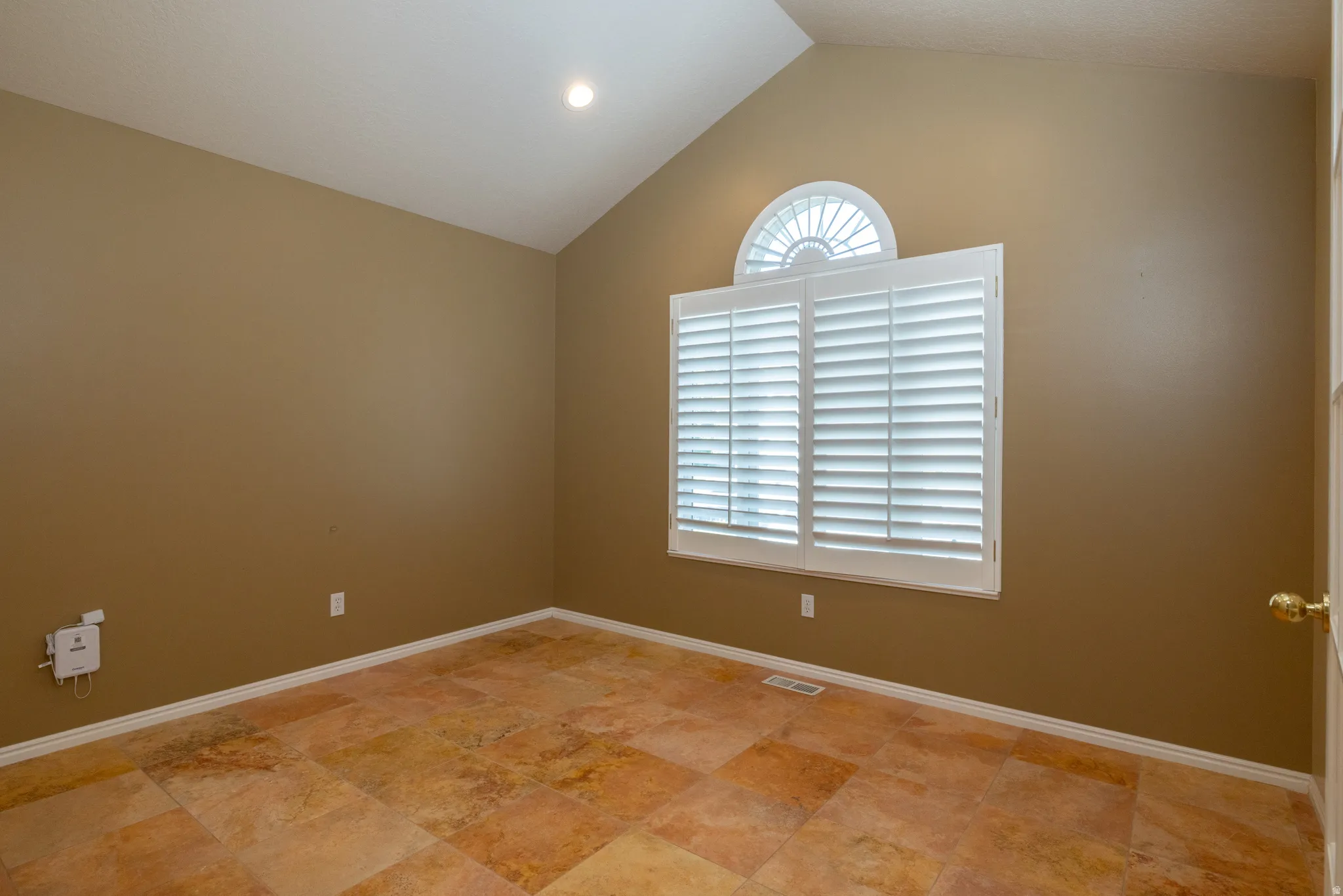 Vaulted ceiling room featuring a large window with plantation shutters and a half-moon transom
