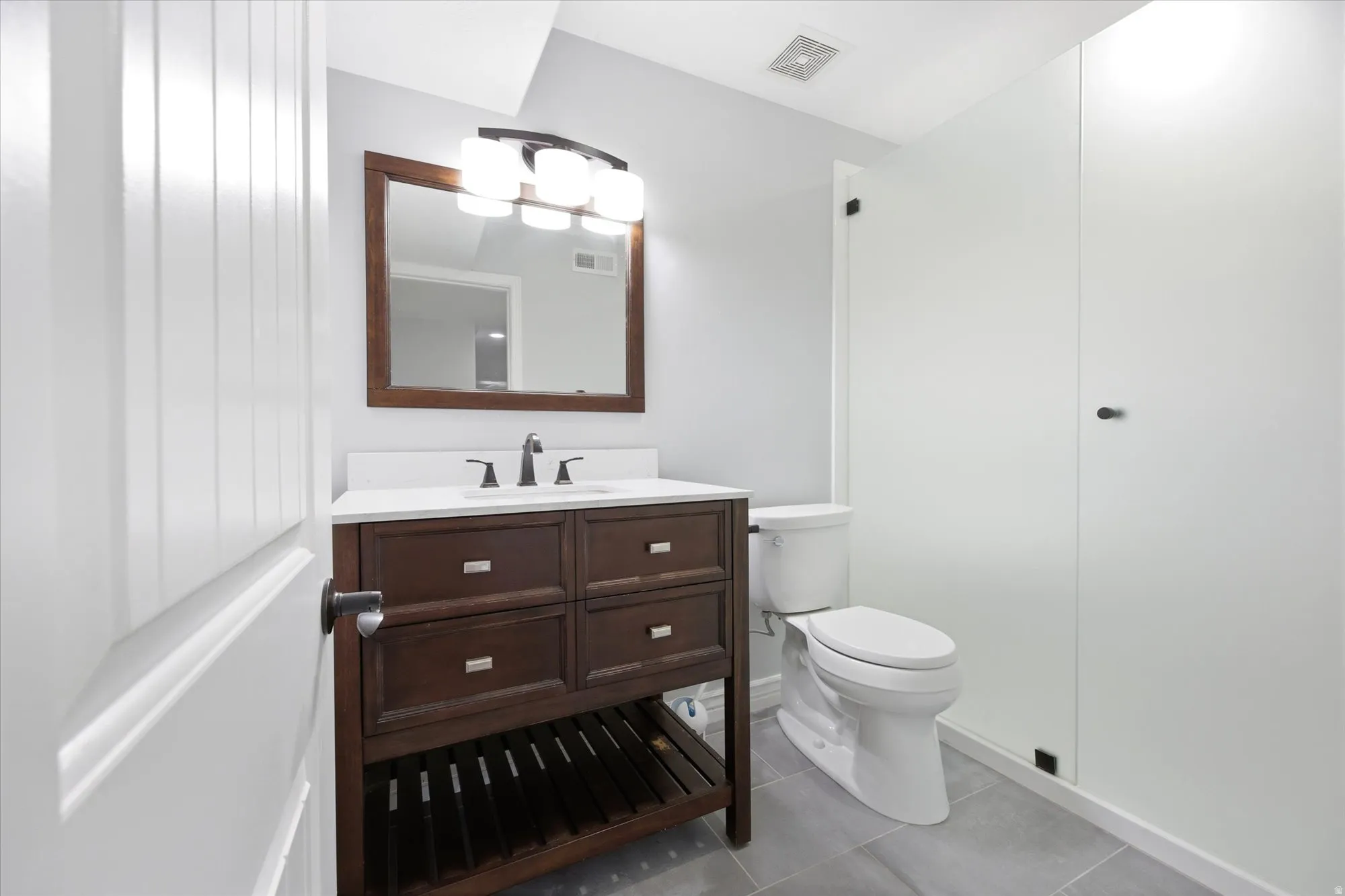 Bathroom featuring a wood-finish vanity with a white countertop and rectangular sink, complemented by a framed mirror and a three-light fixture