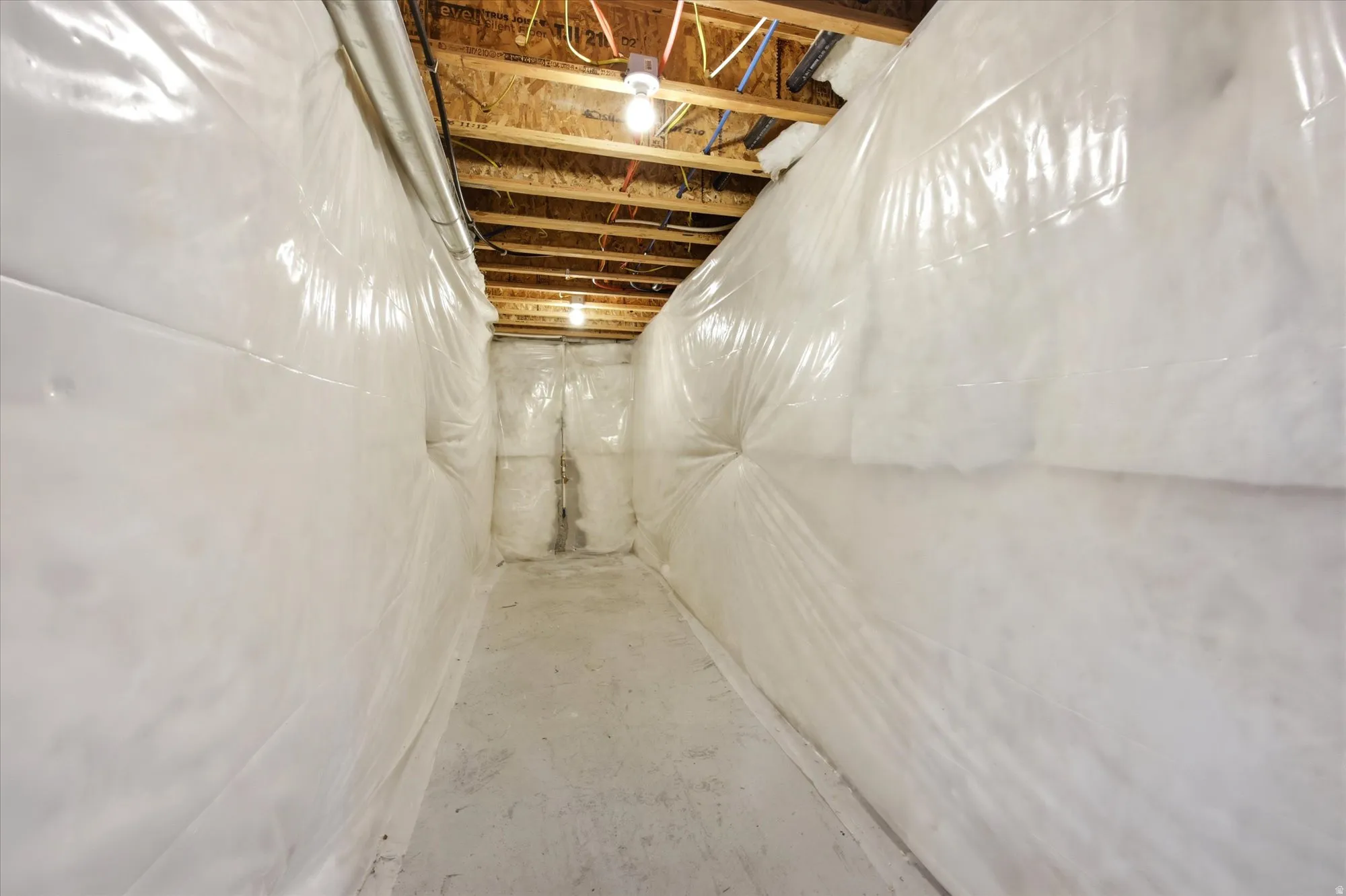 Crawl space featuring white encapsulation lining, exposed wood ceiling joists, and concrete flooring