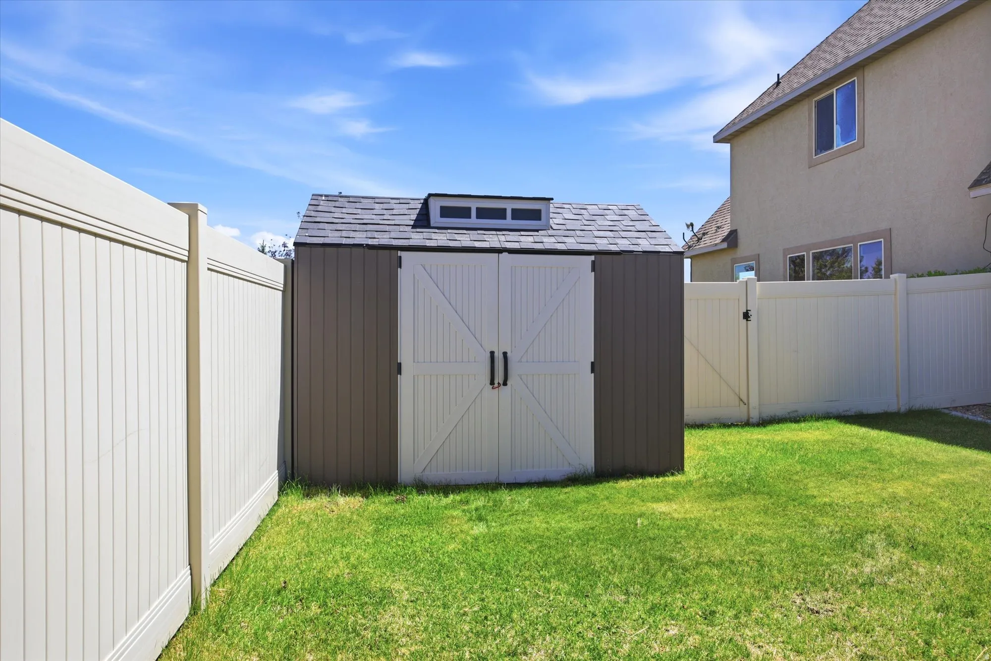 Freestanding outdoor storage shed featuring a gray shingle roof, a dormer with windows, and white barn-style double doors with black hardware