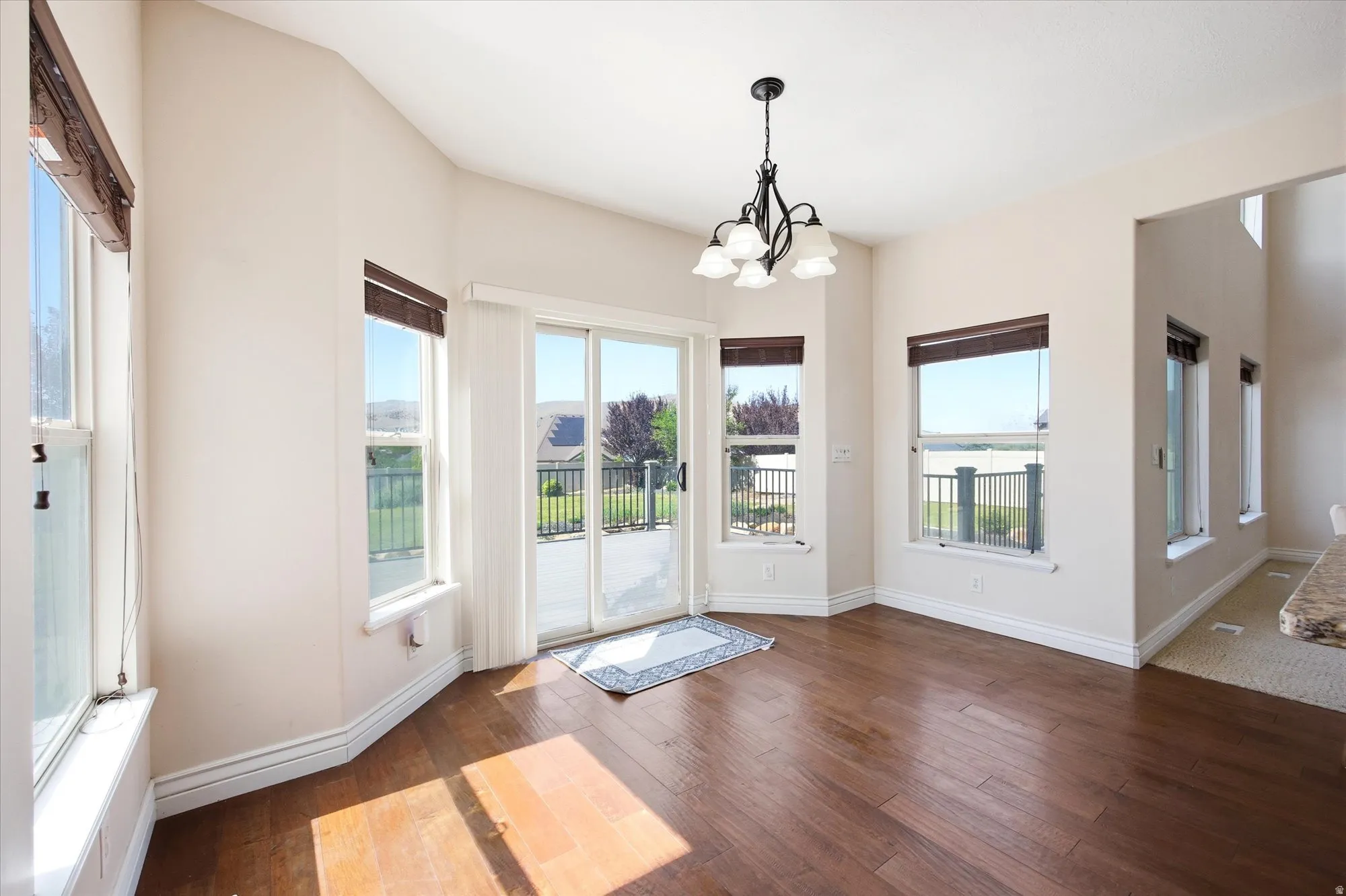 Dining area featuring wood-finish flooring, a contemporary chandelier, multiple windows with blinds, a sliding glass door to an outdoor deck, and white baseboards